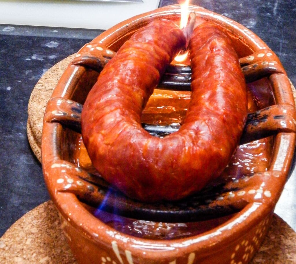 Portuguese chouriço sausage being flame-grilled in a traditional earthenware dish during a Lisbon cooking class.