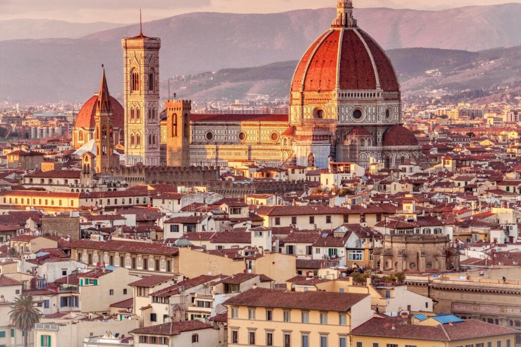 Panoramic view of Florence, Italy, with terracotta rooftops and the large red dome of Florence Cathedral (Duomo) and Giotto’s Bell Tower standing prominently against the Tuscan hills.