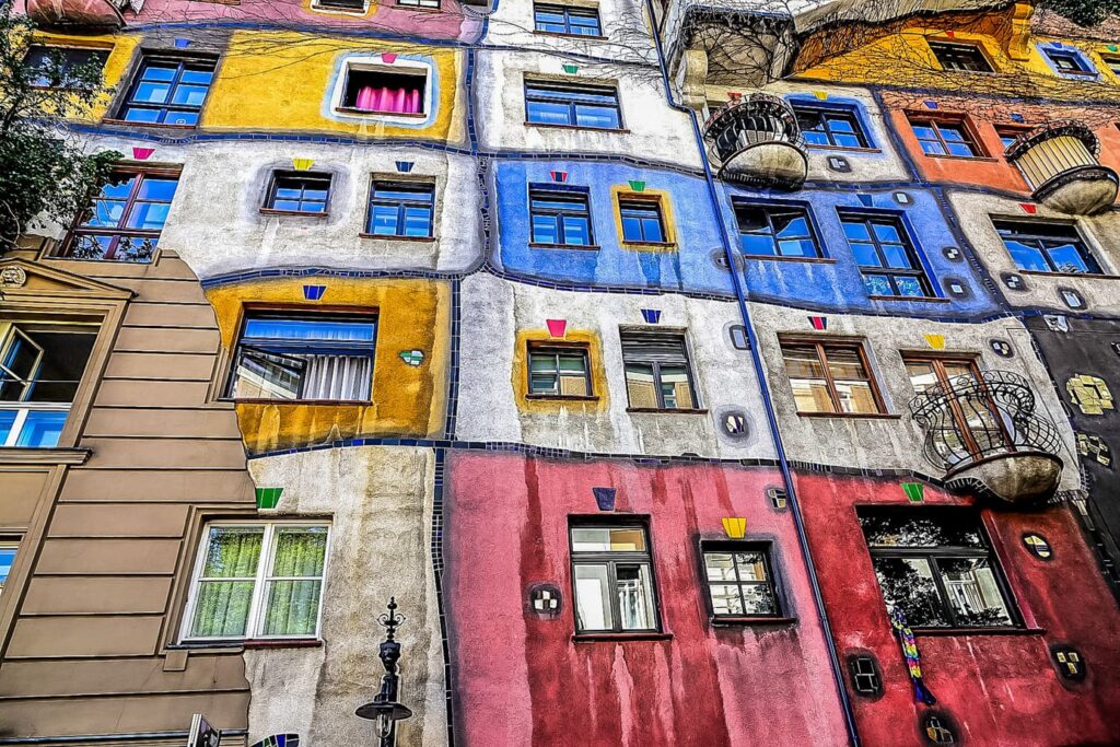 Colourful façade of the Hundertwasserhaus in Vienna with uneven windows, bright paintwork, and greenery growing from the balconies.