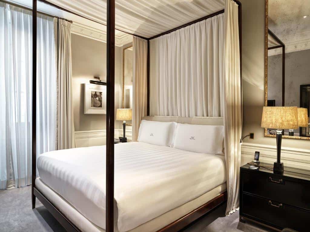 Elegant four-poster bed at J.K. Place Roma with soft neutral tones, mirrored walls, and warm lighting creating a refined, intimate atmosphere.