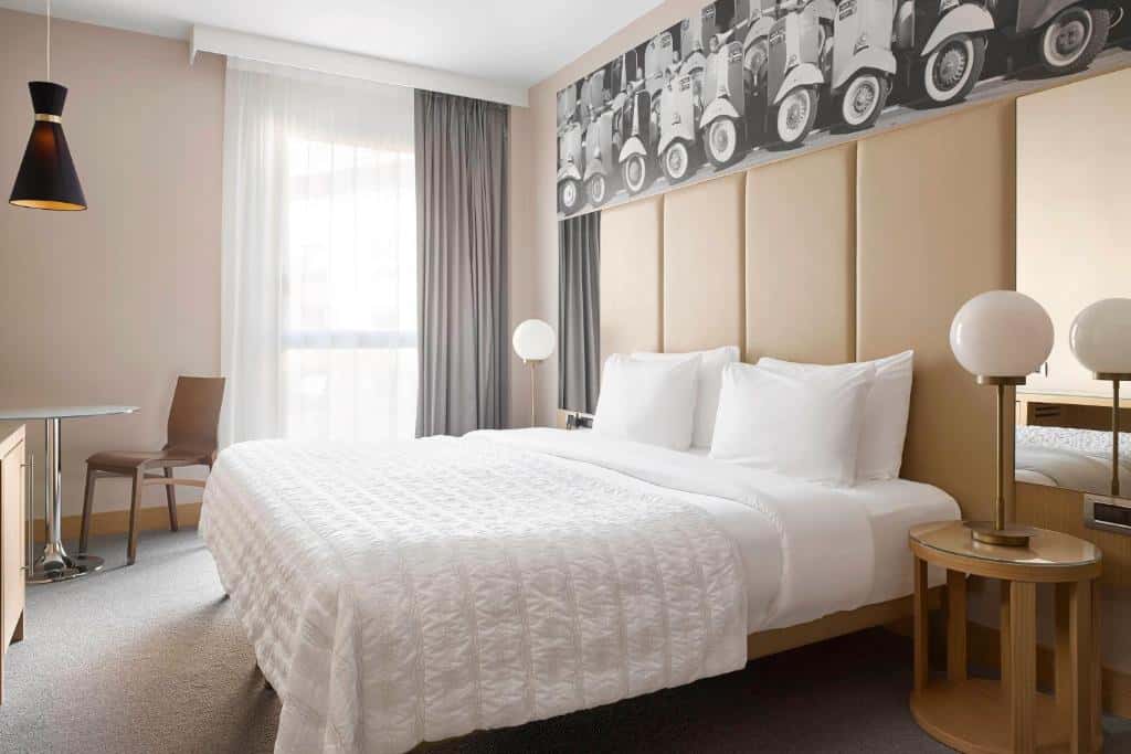 Bright, stylish bedroom at Le Méridien Visconti Rome featuring clean modern design, neutral tones, and a Vespa-themed mural.