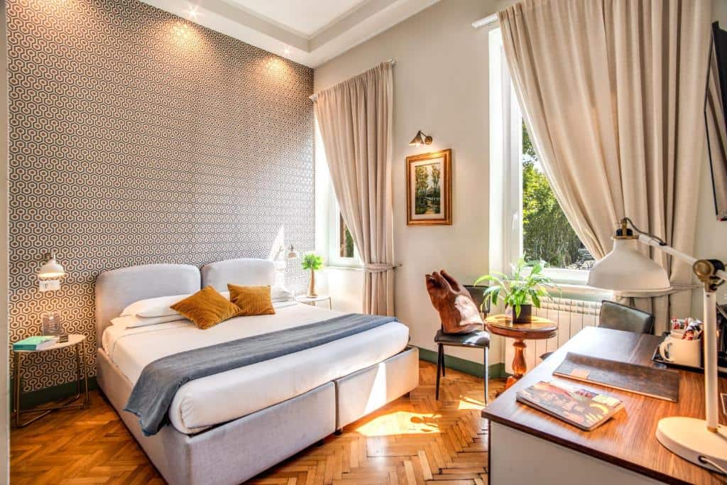Bright boutique bedroom at Tree Charme Trilussa Palace Hotel Rome with patterned wallpaper, sunlight streaming through tall windows, and cosy mid-century décor.