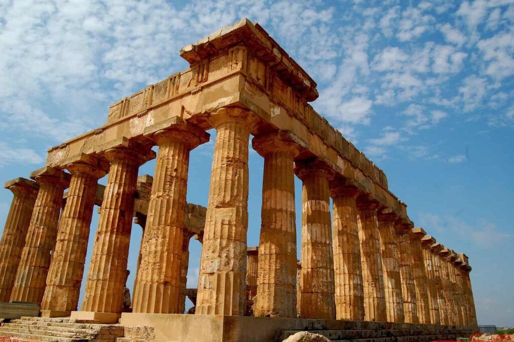 Ancient Greek temple ruins at the Valley of the Temples in Agrigento, Sicily, surrounded by olive trees and blue sky.