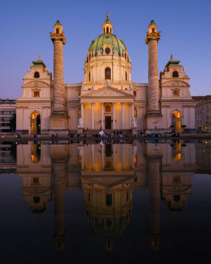 Karlskirche in Vienna with its striking green dome and twin columns reflected in the pool at Karlsplatz.