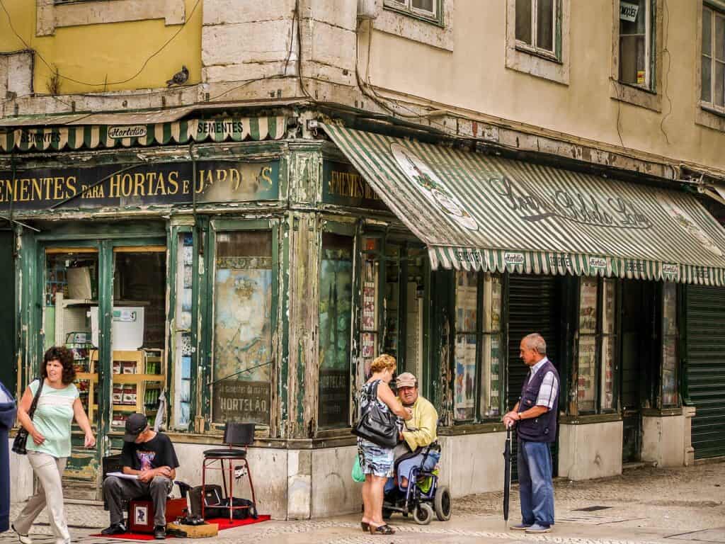 Historic Lisbon storefront with green striped awning and locals chatting outside, part of the city’s Lojas com História heritage shops.