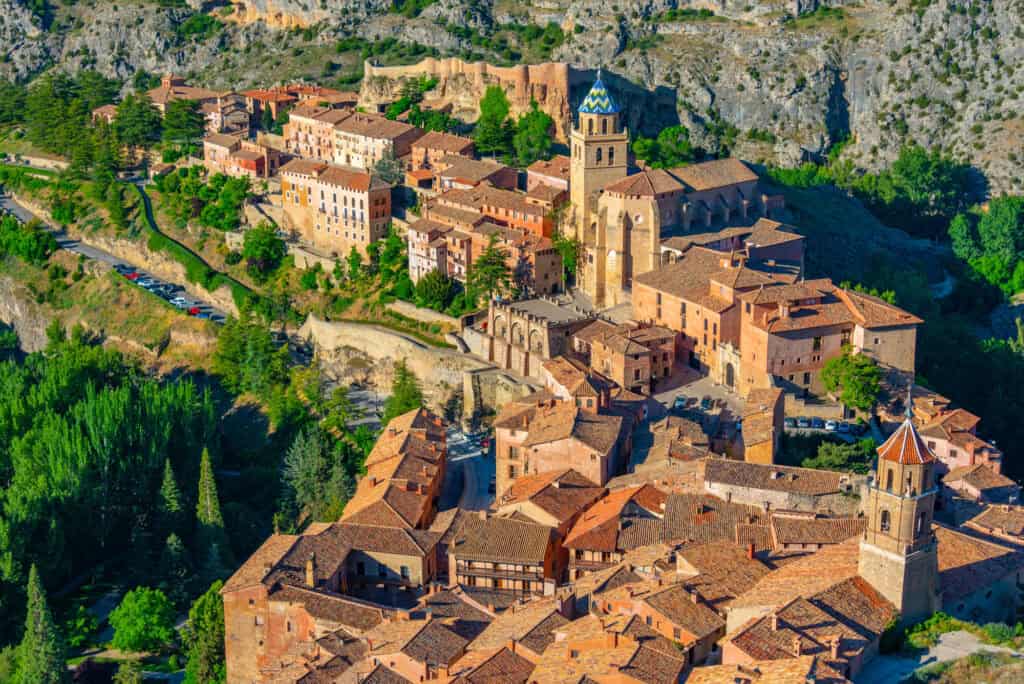 Panoramic view of Albarracín, Spain, with pink stone houses, medieval walls and towers set against rugged hills.”