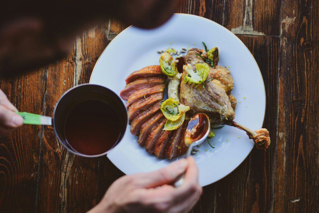 Duck confit with crispy skin served with roasted vegetables on a white plate