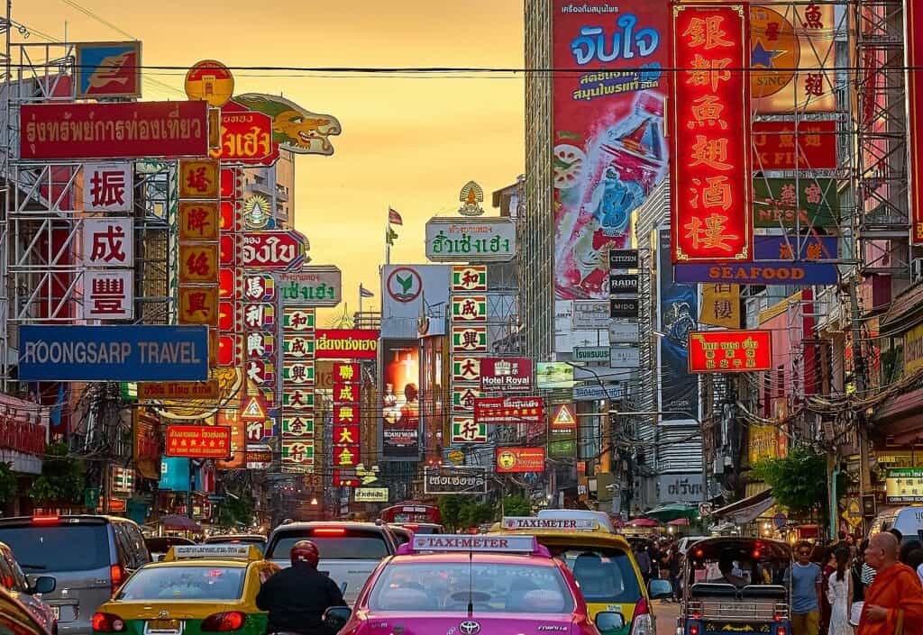 Busy Bangkok Chinatown street with neon signs, traffic and crowded Yaowarat Road at sunset