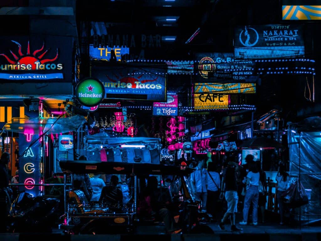 Neon-lit Bangkok street in Silom at night with bars, tuk-tuks and pedestrians under glowing signs