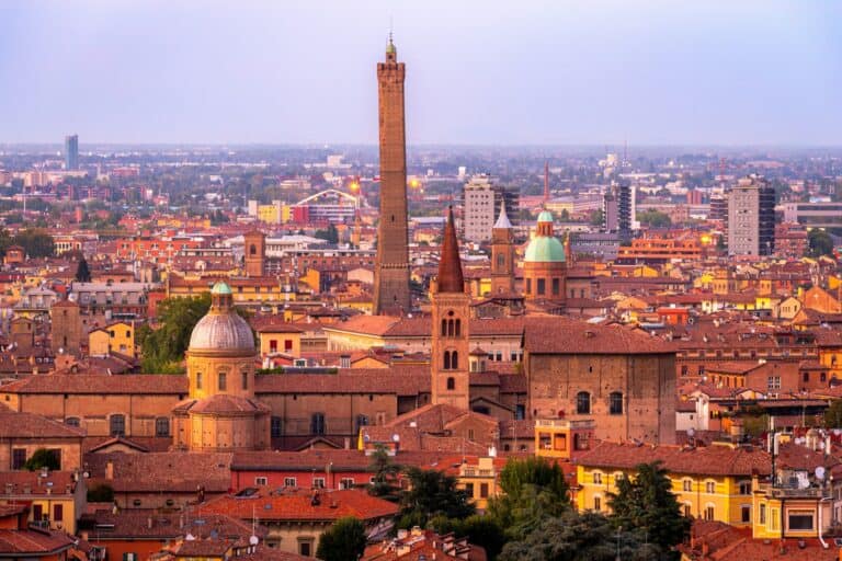 “Aerial view of Bologna’s red rooftops and medieval towers with the hills in the distance.