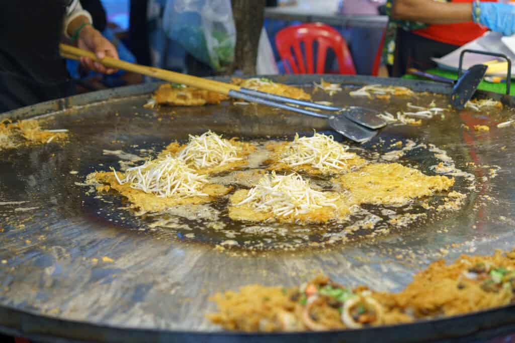 Hoy Tod oyster omelettes cooking on a large hotplate at a Bangkok street food stall in Chinatown