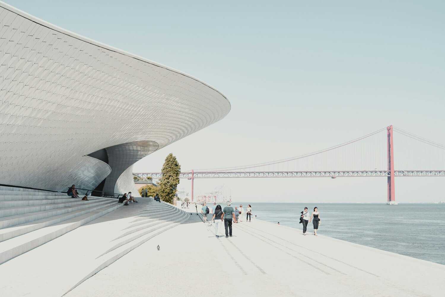 MAAT Museum in Lisbon with modern curved architecture beside the Tagus River and the 25 de Abril Bridge in the background