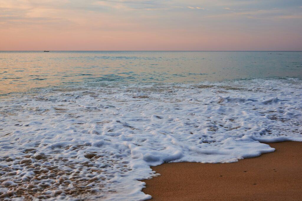 Mai Khao Beach Phuket at sunset with gentle waves washing onto the sandy shoreline